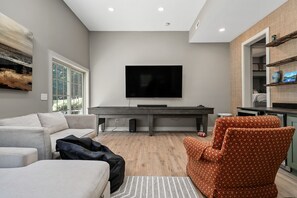 A modern living room with a flat-screen TV, a sofa, a patterned armchair, and a dining table.