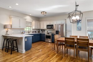 A modern kitchen with a central island, built-in appliances, and a dining area with wooden chairs.