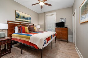 A bedroom with a bed, a nightstand, a dresser, a ceiling fan, and a window with blinds.