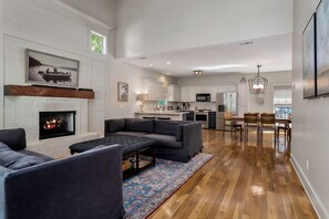 Un salon moderne avec une cheminée, un coin repas avec des meubles en bois et une cuisine équipée d’appareils électroménagers en acier inoxydable.