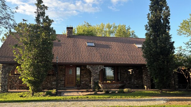Une maison en pierre avec un toit en briques, un porche à l’avant et une pelouse bien entretenue.