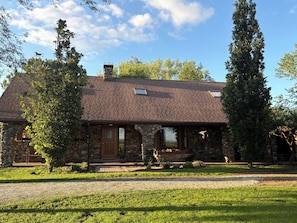 A stone house with a brick roof, a front porch, and a well-maintained lawn.