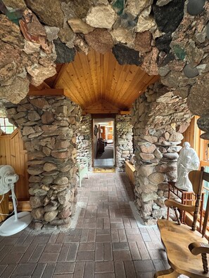 A stone archway leading to a wooden interior with a brick floor and a fan.