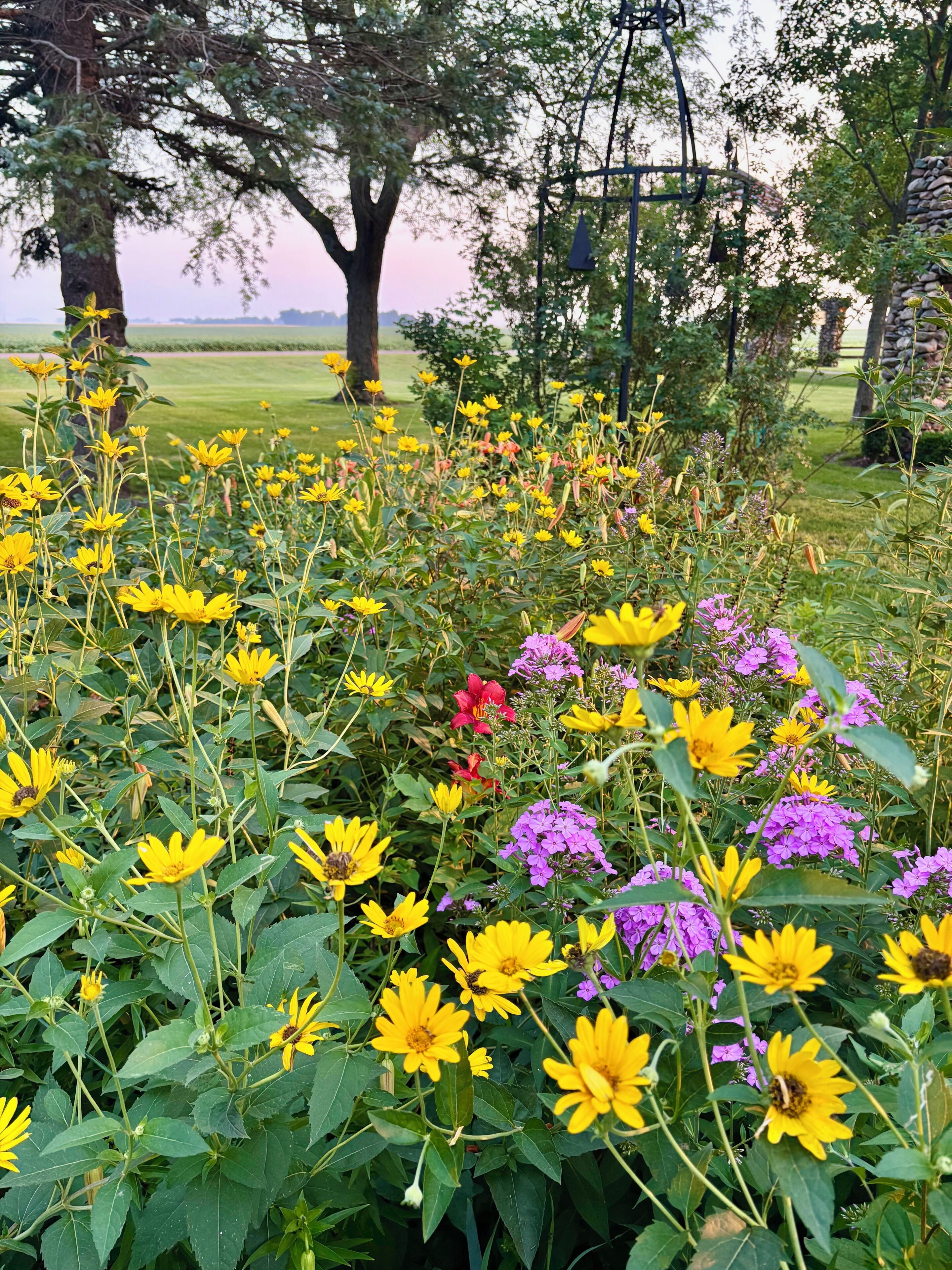 A garden with a variety of flowers, trees, and a stone wall.