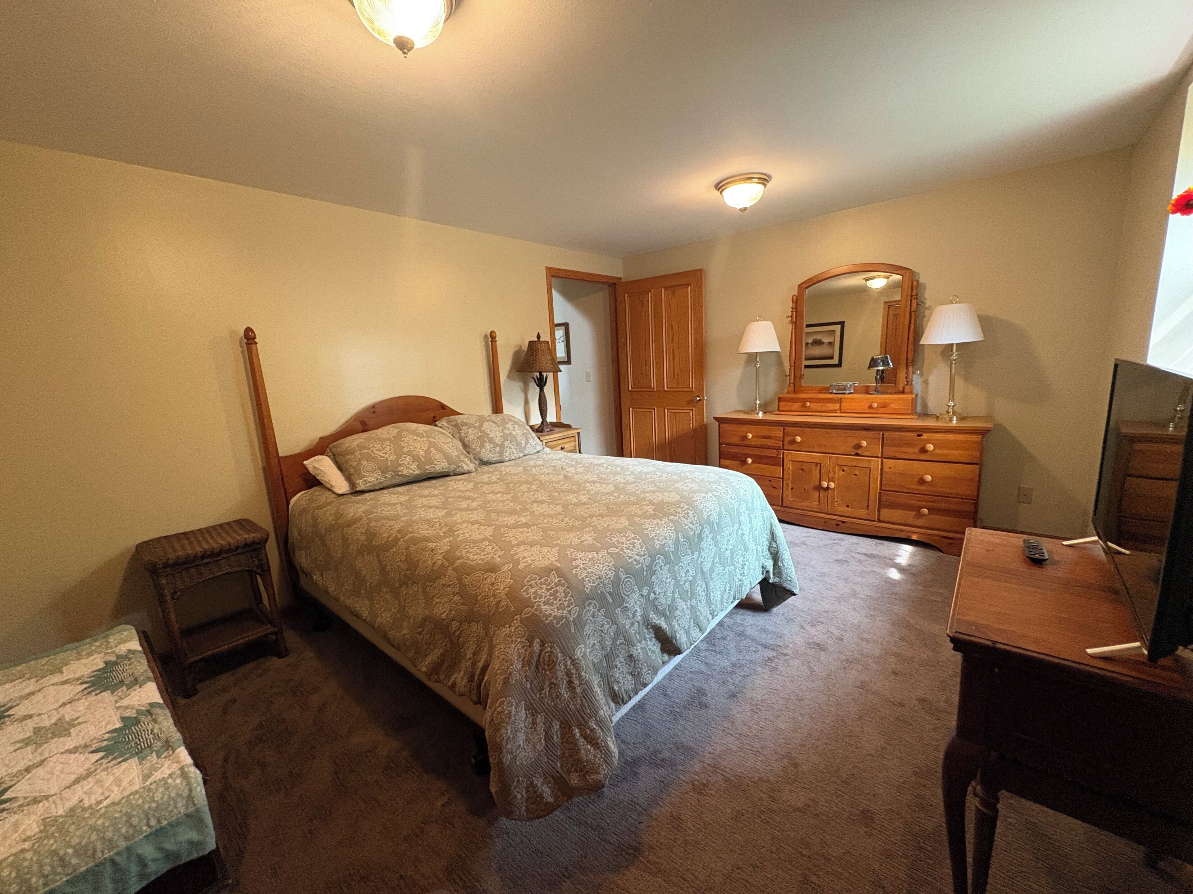 A bedroom with a four-poster bed, a wooden dresser, a mirror, and a television on a wooden stand.