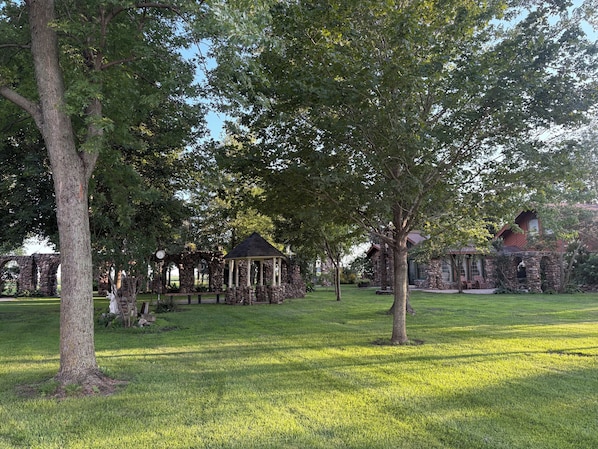 A gazebo surrounded by stone walls and trees in a well-maintained grassy area.
