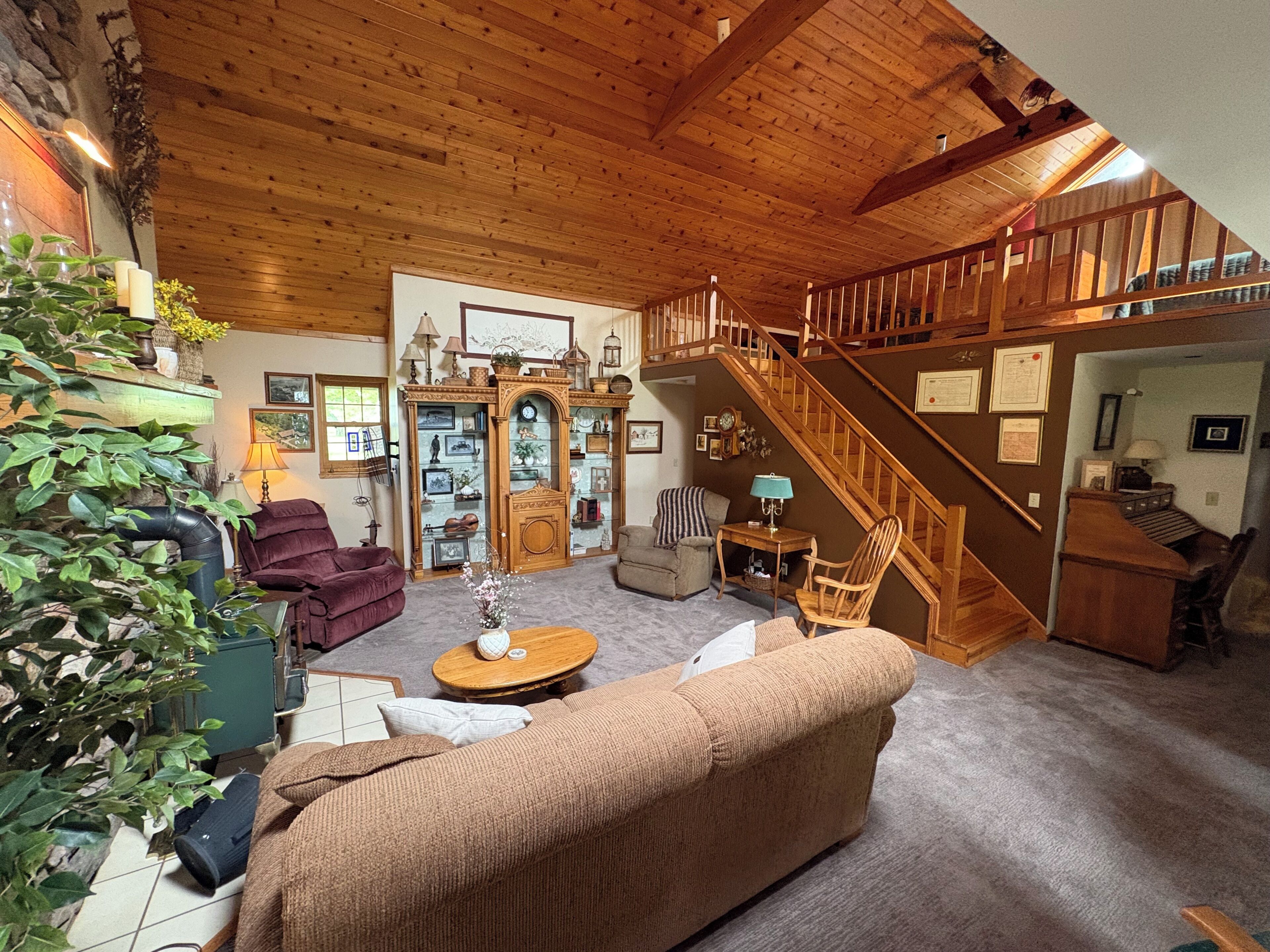 A cozy living room with a wooden ceiling, a staircase, a sofa, a coffee table, and a bookshelf.