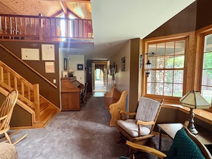 A spacious hallway with a wooden staircase, multiple seating areas, and a large window providing a view of the outdoors.