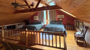 Une chambre avec deux lits, des poutres en bois, un escalier en bois et une vue sur l’extérieur.