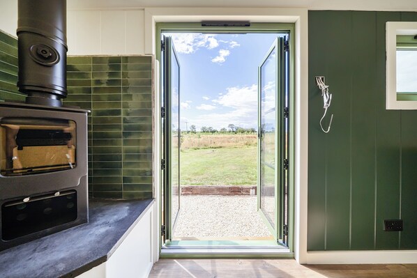 Una cocina con estufa de leña empotrada, salpicadero de azulejos verdes y puerta corrediza de vidrio que da a un espacio al aire libre.