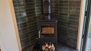 A corner room with a built-in wood stove, a small storage space below, and a view through a glass door.
