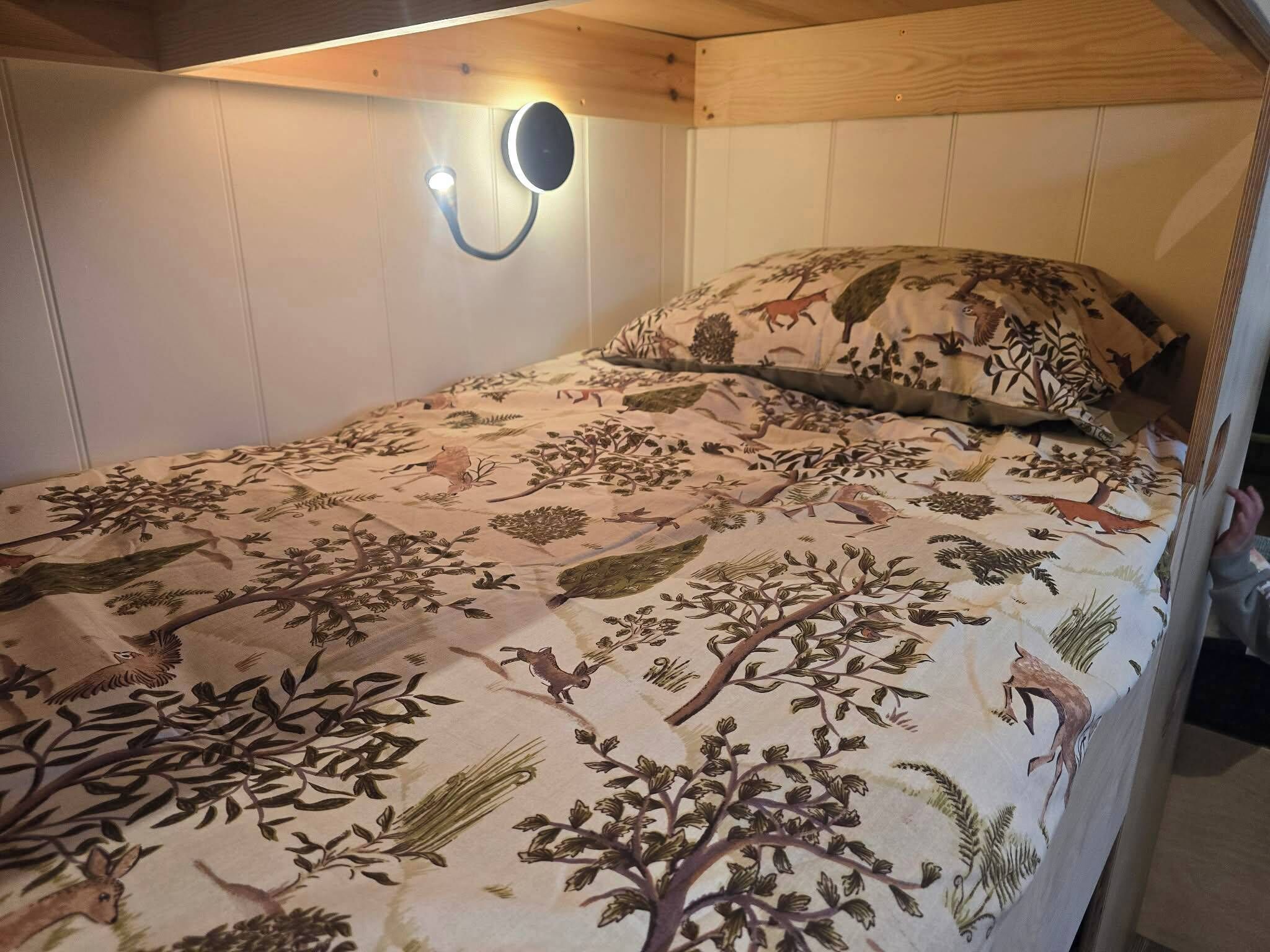 A single bed with a floral-patterned bedspread, a wall-mounted light fixture, and a wooden headboard.