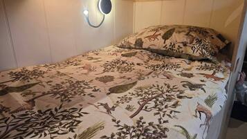 A single bed with a floral-patterned bedspread, a wall-mounted light fixture, and a wooden headboard.