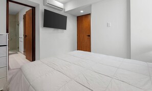 A bedroom with a bed, a television mounted on the wall, a wardrobe, and a door leading to a bathroom. - Maralma Bucerías Retreat | Rooftop, Pool + Terrace (Bucerías)
