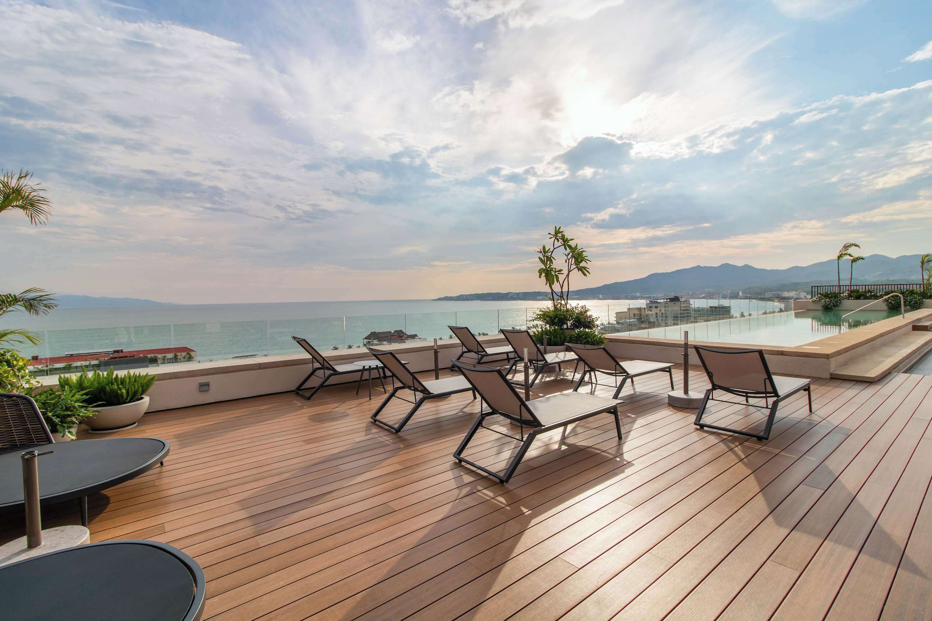 A wooden deck with lounge chairs and a pool overlooking a body of water and mountains.