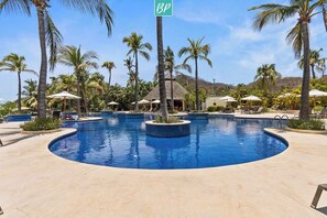 Ein Poolbereich eines Resorts mit Palmen, Liegestühlen und Sonnenschirmen.