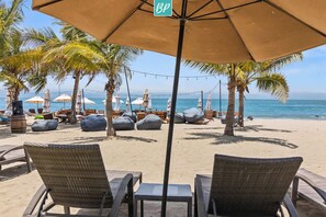 Eine Strandlounge mit Korbmöbeln, einem Tisch und einem großen Sonnenschirm.