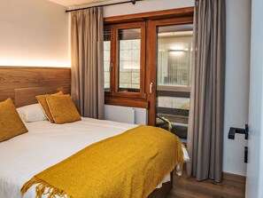 Ein Hotelzimmer mit Bett, Holz-Kopfteil, Fenster mit Vorhängen und Blick nach draußen.