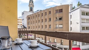 En balkong med ett bord dukat för två personer, med utsikt över en stadsbild med byggnader och ett klocktorn.