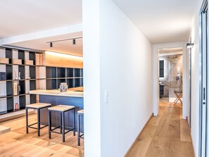 A modern kitchen with a bar area, wooden flooring, and a view into the adjacent living space. - Chesa Zentrum 10B by Interhome (St. Moritz)