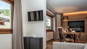 Ett modernt vardagsrum med en platt-TV som är monterad på väggen, en matplats med bord och stolar samt ett stort fönster med gardiner.