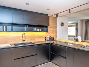 Une cuisine moderne avec des meubles de couleur sombre, un plan de travail en bois et une cuisini ère intégrée.