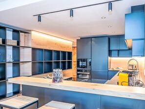 Eine moderne Küche mit einer zentralen Kochinsel, eingebauten Regalen und einem Edelstahlkühlschrank.