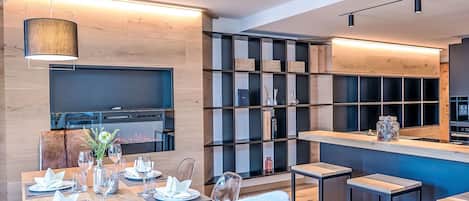 Un comedor moderno con una mesa de madera dispuesta para una comida, una zona de bar con taburetes y una cocina al fondo.