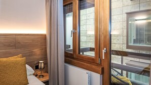 Ett hotellrum med en säng, ett nattduksbord, en lampa, ett fönster med gardiner och utsikt över balkongen.