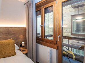 Ein Hotelzimmer mit Bett, Nachttisch, Lampe, einem Fenster mit Vorhängen und Blick auf den Balkon.
