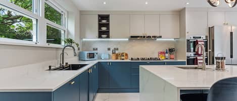 A modern kitchen with a central island, built-in appliances, and a window overlooking greenery.
