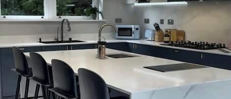 A modern kitchen with a marble island, black bar stools, and a large window.