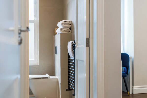 A bathroom with a toilet, a towel rack with folded towels, and a window.