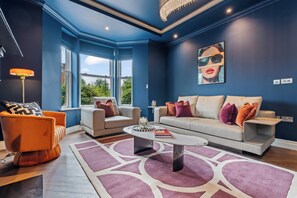 Ein modernes Wohnzimmer mit blauer Akzentwand, einer Sofagarnitur, einem Couchtisch und einem gemusterten Teppich.