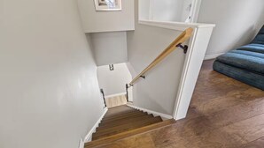 En trappa med trästeg och ett ledstång, som leder upp till en liten plattform med en vit vägg och ett fönster.