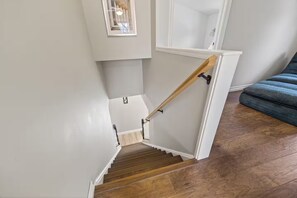 Un escalier avec des marches en bois et une rampe, menant à un palier avec un mur blanc et une fenêtre.