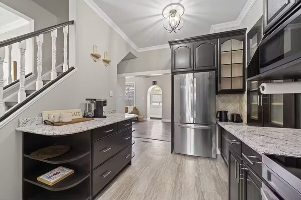 A modern kitchen with dark cabinetry, a stainless steel refrigerator, and a marble countertop.