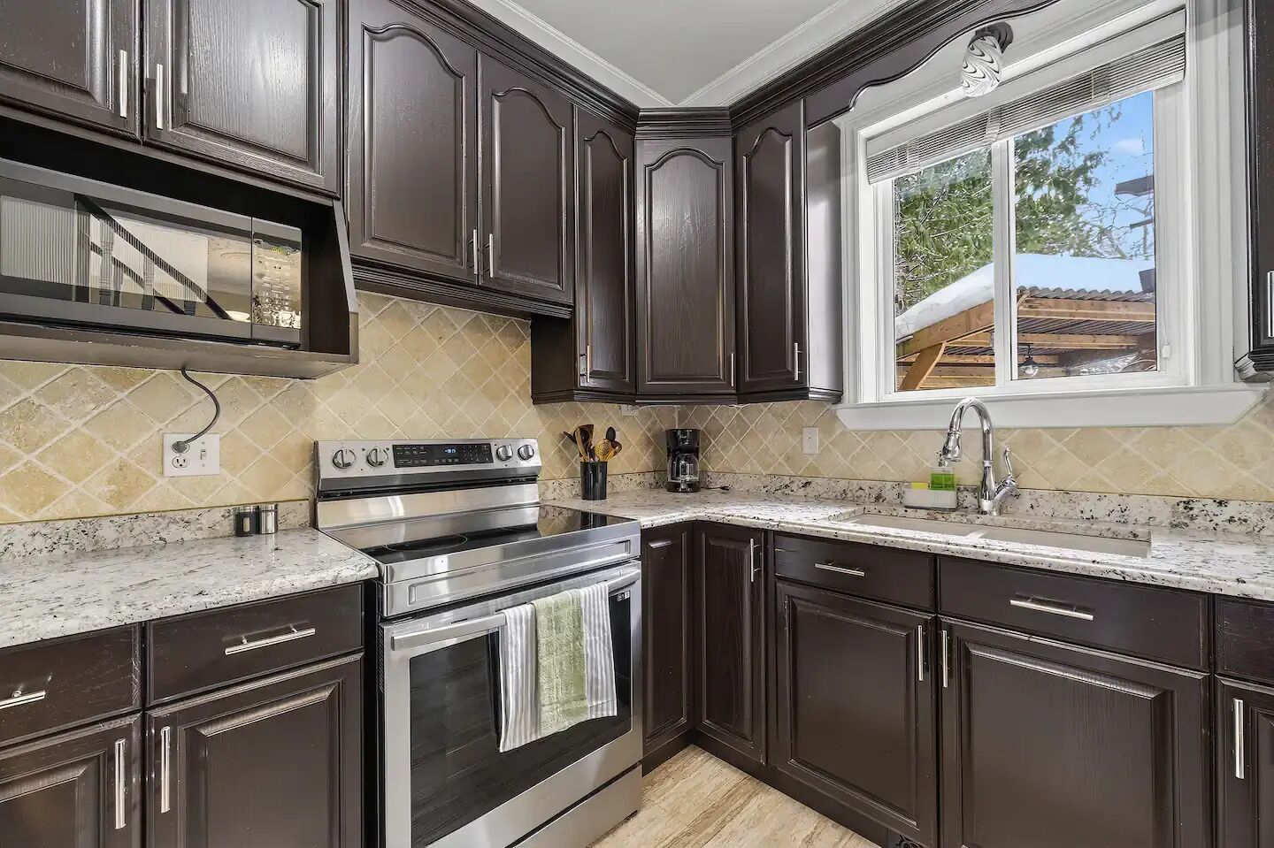 A kitchen with dark wood cabinets, a stainless steel stove, and a window with a view of the outside.