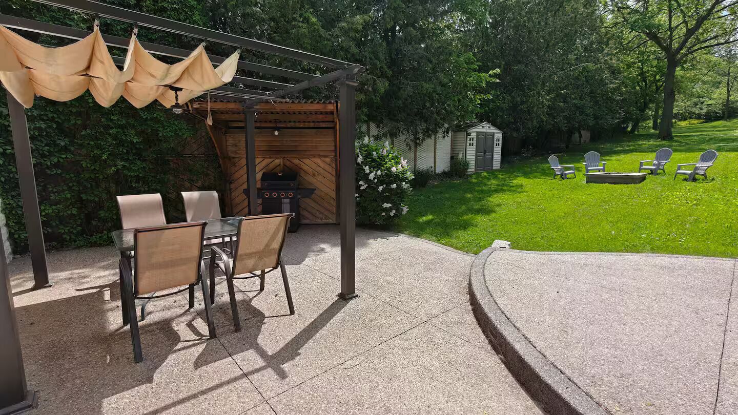 Une terrasse extérieure équipée d’un barbecue, de chaises et d’une pergola agrémentée de coussins suspendus.