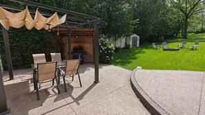 An outdoor patio with a grill, chairs, and a pergola with hanging cushions.