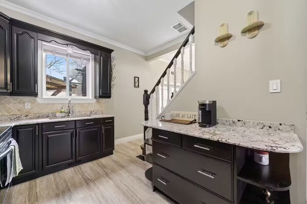 A kitchen with dark cabinetry, a marble countertop, and a coffee maker.