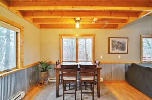 A dining area with a wooden table and chairs, a window with a view of trees, and a framed picture on the wall. - Brook Side Cabin (Crosslake)