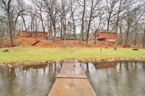 A wooden deck leading to a pond with a small bridge, surrounded by trees and two buildings.