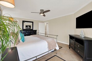 A bedroom with a bed, a dresser, a ceiling fan, a mirror, and a television on the wall. - Colorful Oceanfront Escape on Tybee's South End | Heated Pool Access (Tybee Island)