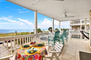 A covered outdoor area with a table set for dining, chairs, and a view of the ocean. - Colorful Oceanfront Escape on Tybee's South End | Heated Pool Access (Tybee Island)