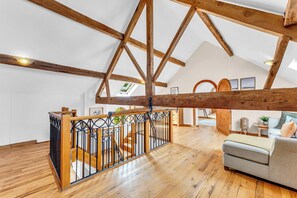 Ein geräumiger Lofts mit hohen Decken, freiliegenden Holzbalken, einer Holztreppe und einer gemütlichen Sitzecke mit Sofa und Kissen.