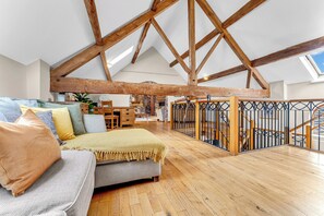 A loft-style room with exposed wooden beams, a sofa, and a staircase with a metal railing. - Luxury Stay Sleeps 14 Near M 6 (Newcastle Under Lyme)