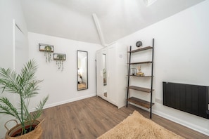 A hallway with wooden flooring, white walls, and a black radiator. There are two wall-mounted shelves with decorative items and a mirror reflecting a room. - Luxury Apartment6 - City Centre Manchester (Manchester)