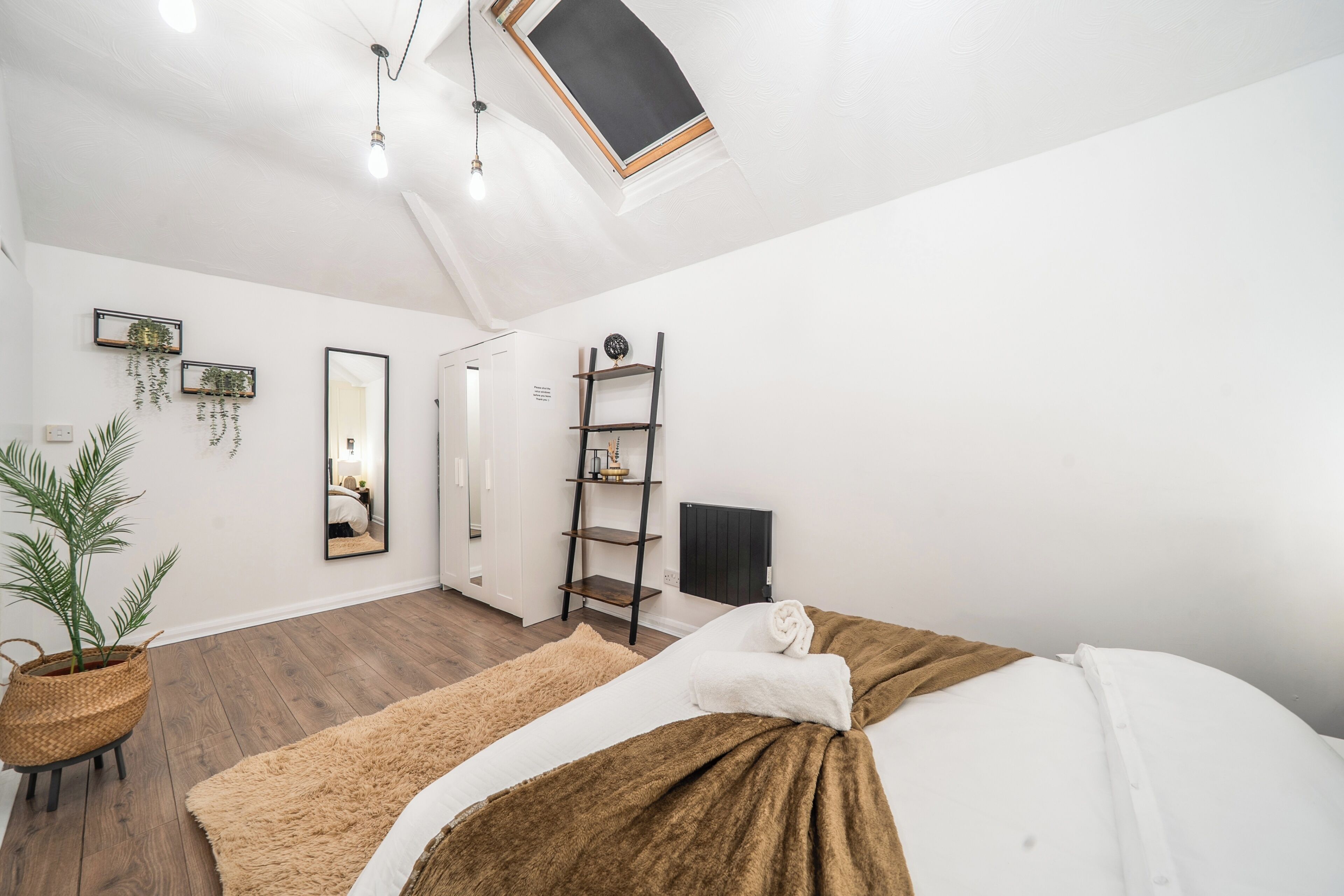 A modern bedroom with a bed, a mirror, a shelf, and a potted plant.