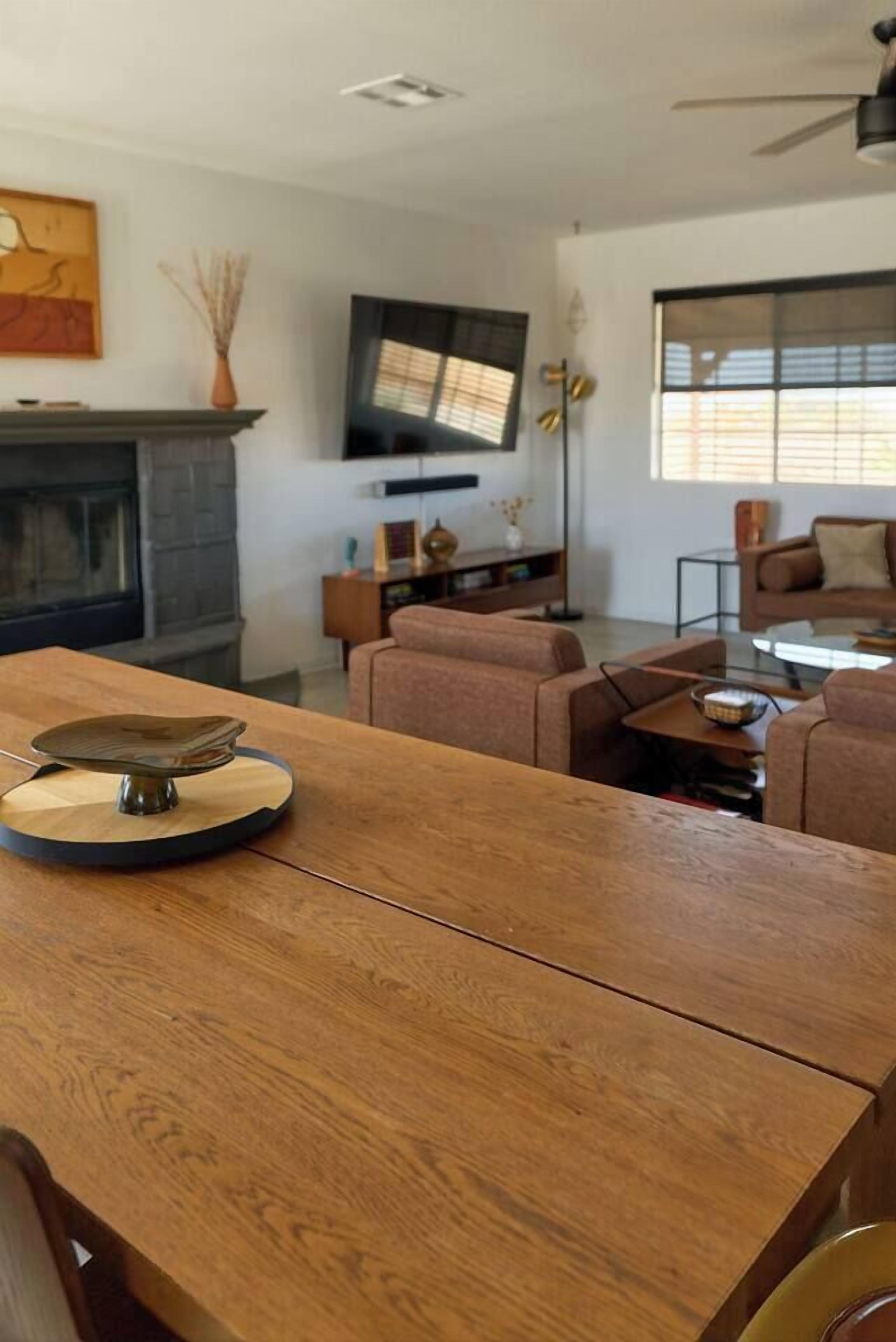 A modern living room with a wooden dining table, sofas, a fireplace, and a television.